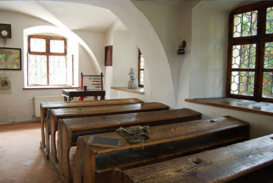 Prima Scoala Romaneasca se află în interiorul curții Bisericii Sfântul Nicolae din cartierul istoric Șcheii Brașovului.